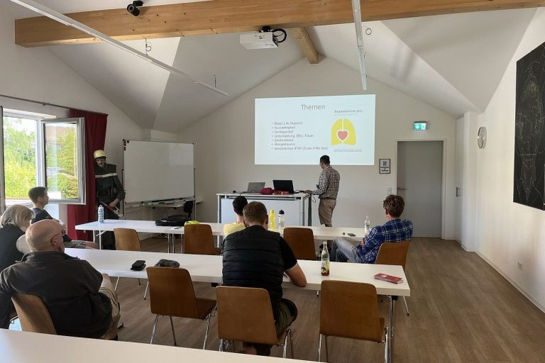 In einem Seminarraum hören Erwachsene Menschen einem Trainer zu.